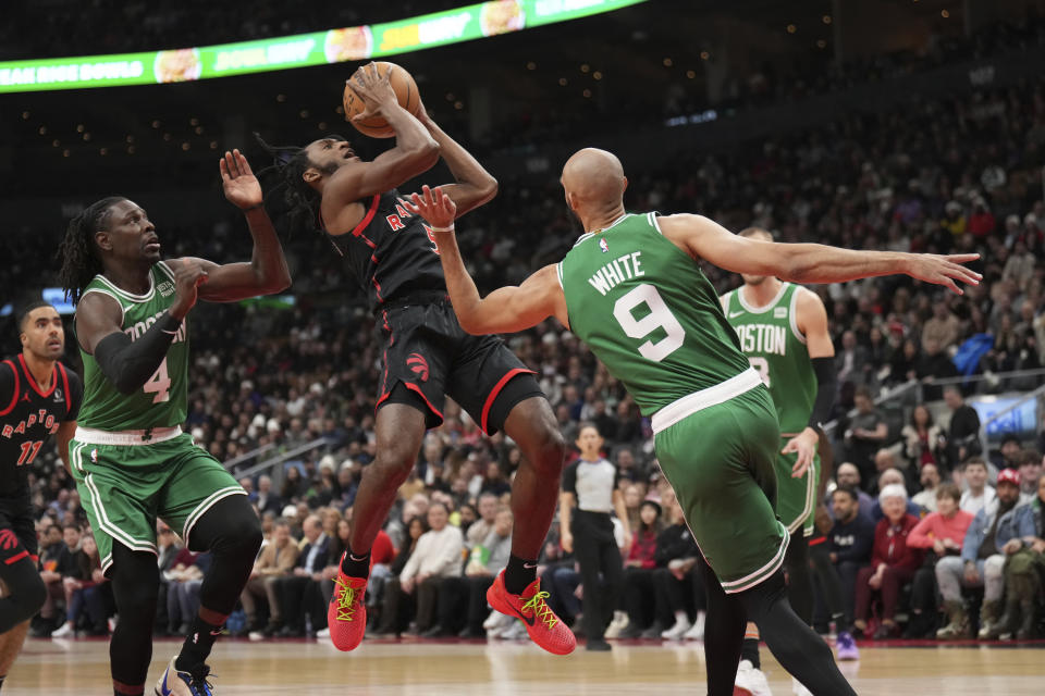 Toronto Raptors guard Immanuel Quickley (5) goes up to shoot as Boston Celtics guards Derrick White (9) and Jrue Holiday (4) defend during first-half NBA basketball game action in Toronto, Monday Jan. 15, 2024. (Nathan Denette/The Canadian Press via AP)