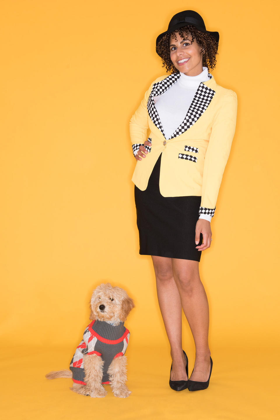 A woman in a dress suit and hat standing with a dog