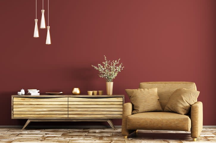 tan-leather-chair-sits-next-to-a-tan-credenza-against-a-brick-red-wall-and-a-pendant-light-fixture-overhead