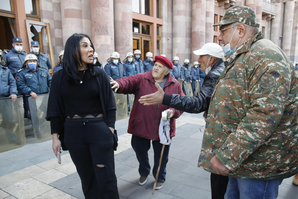 People argue as the police officers guard in front of the government building in Yerevan, Armenia, Tuesday, Nov. 10, 2020. Thousands of people streamed to the main square in the Armenian capital early Tuesday to protest the agreement to halt fighting over the Nagorno-Karabakh region, many shouting "We won't give up our land." Some of them broke into the main government building, saying they were searching for Pashinian, who apparently had already departed. (AP Photo/Dmitri Lovetsky)