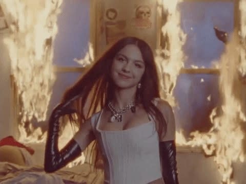 Olivia Rodrigo tossing her hair and smiling in a room that's on fire