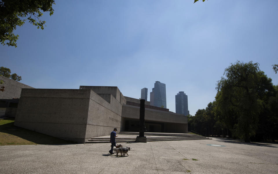 A man walks dogs past the Rufino Tamayo Museum in Mexico City, Tuesday, March 24, 2020. Beginning Monday, Mexico's capital shut down museums, bars, gyms, churches, theaters, and other non-essential businesses that gather large numbers of people, in an attempt to slow the spread of the new coronavirus. (AP Photo/Fernando Llano)