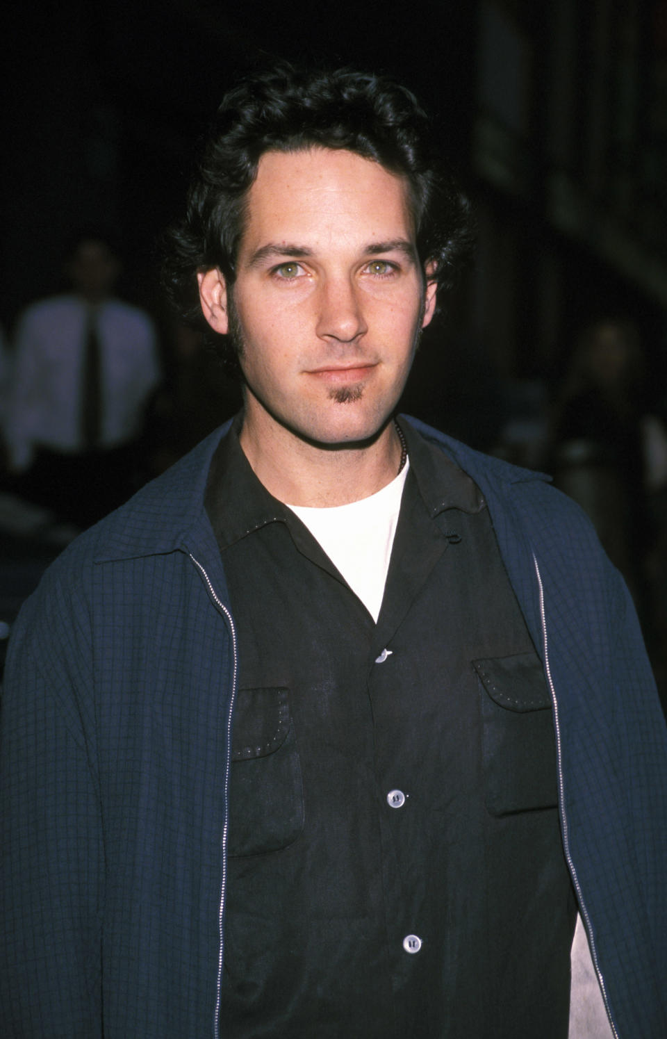 Paul Rudd at an event, wearing a casual dark shirt with a white undershirt, and a jacket