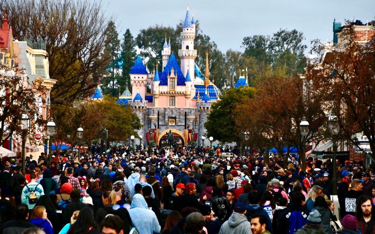 A large crowd throngs the park, with a fanciful castle visible behind