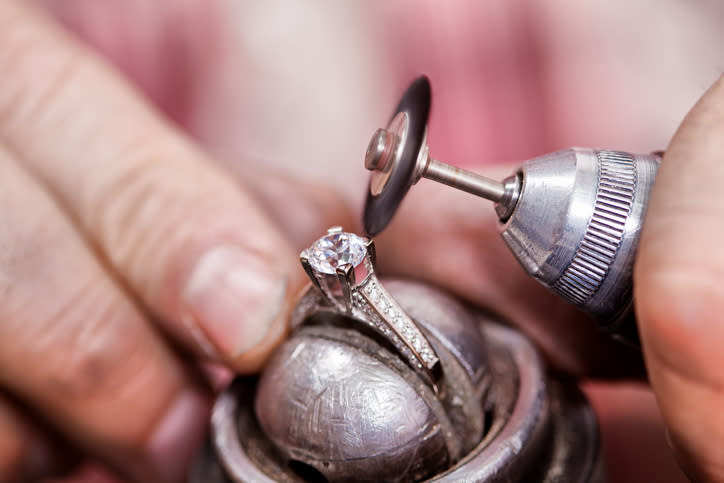 A close-up of hands using a polishing tool on a diamond ring, highlighting the craft of jewelry making