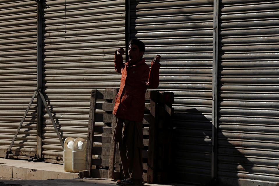A boy yawns as he stands in the sunlight to warm himself in front of closed shops early morning in Karachi
