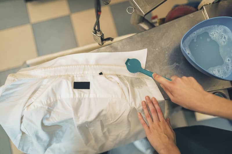 Young female worker in dry-cleaning salon removing stain from white shirt.