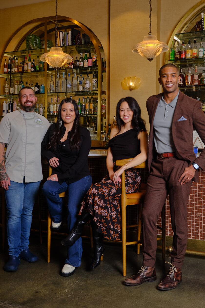 A portrait of four people at a bar of a restaurant.