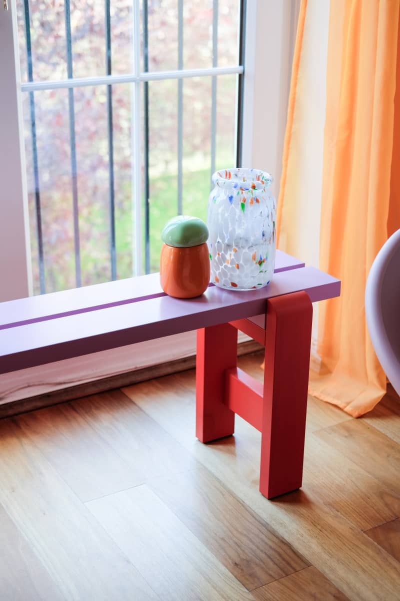 View of red bench in front of window with orange curtain.