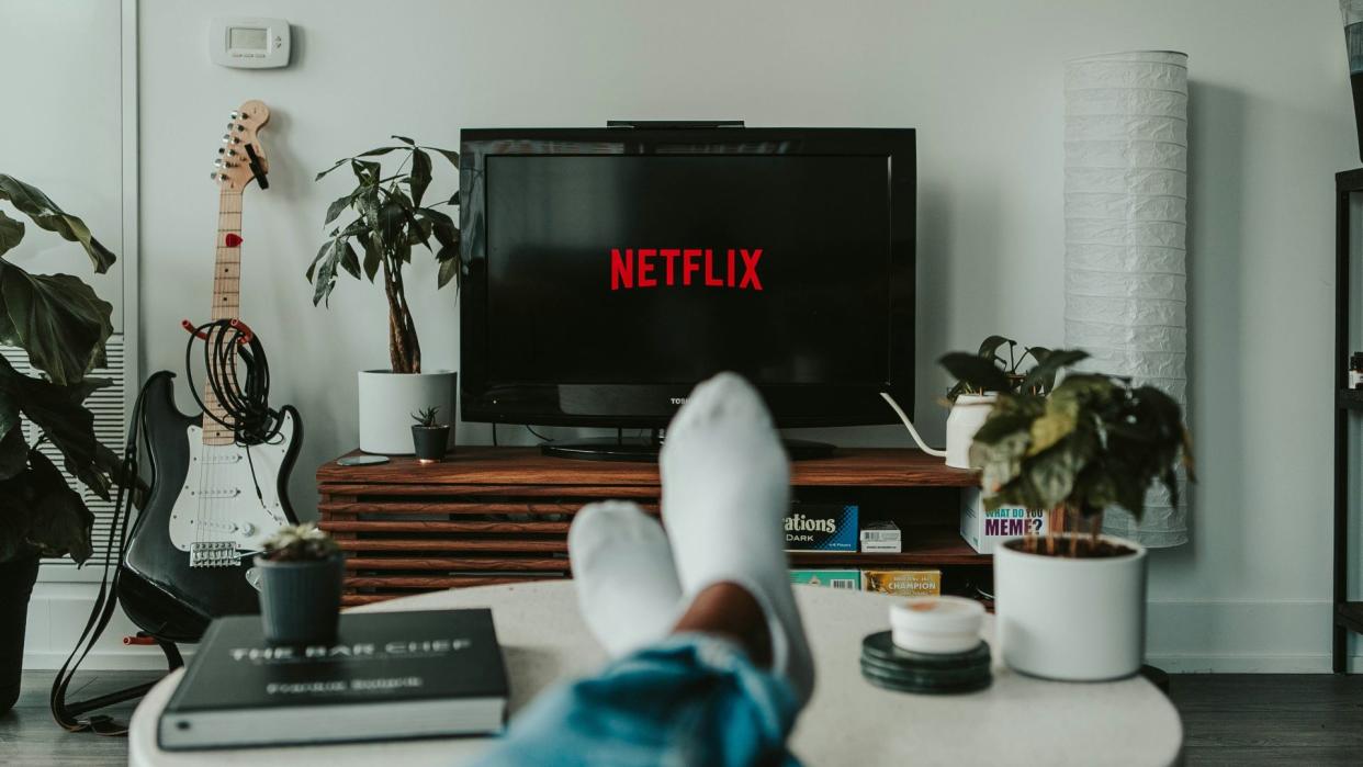  A person sits with their feet up on a coffee table. In the background the Netflix logo is displayed on a TV. 