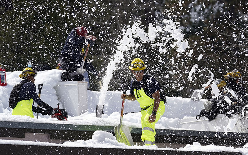 Members of a Cal Fire crew clear snow off the roof of the town's post office after a series of storms