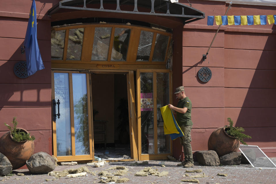 Ukrainian serviceman holds a Ukrainian flag next to the entrance of a restaurant damaged by a Russian attack in Chernihiv, Ukraine, Saturday, Aug. 19, 2023. (AP Photo/Efrem Lukatsky)