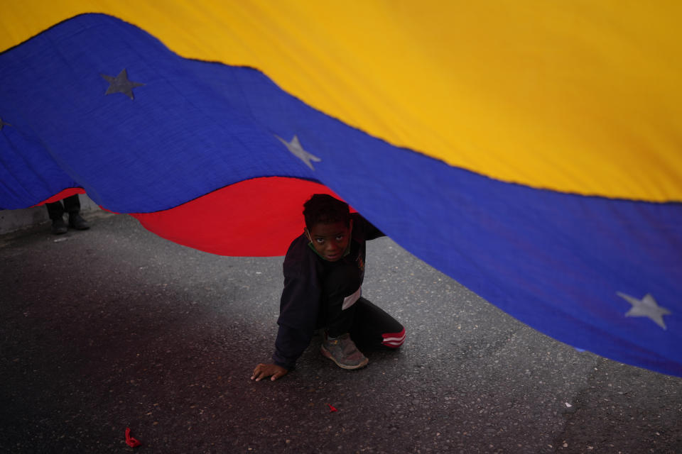 A child plays under a national flag during a march of government supporters marking Youth Day, in Caracas, Venezuela, Saturday, Feb. 12, 2022. The annual holiday commemorates the young people who accompanied heroes in the battle for Venezuela's independence. (AP Photo/Matias Delacroix)