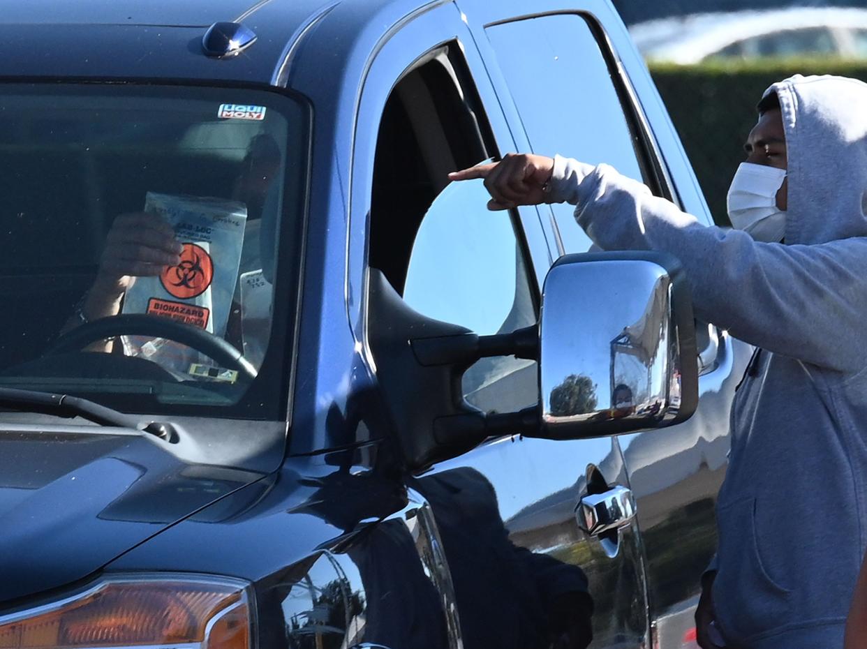 In this file photo taken on 17 November 2020 a Covid-19 testing site staff member explains how to take a self-administered coronavirus test to a person in their car at a drive-up testing site in Los Angeles, California ((AFP via Getty Images))