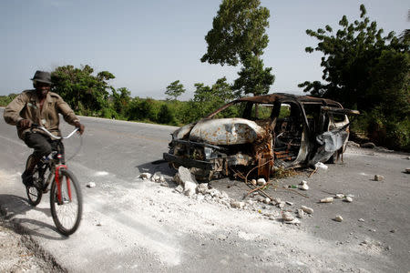 A man rides a bicycle next to a burnt car on the outskirts of Croix-des-Bouquets, Haiti, July 8, 2018. REUTERS/Andres Martinez Casares