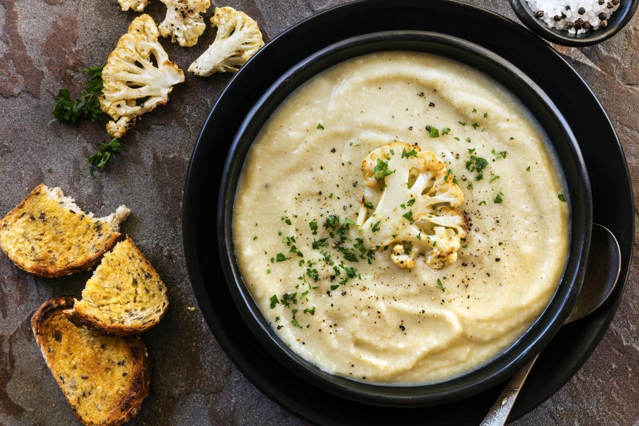 Roasted cauliflower soup in rustic black bowl, with crusty sourdough toast.  Top view.