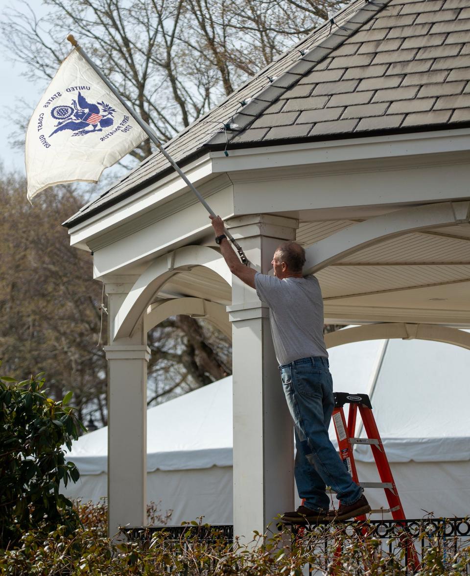 Volunteer Mike Whalen places military branch flags on the gazebo on the Hopkinton Town Common as the start line for the 127th Boston Marathon was being painted, April 11, 2023. 