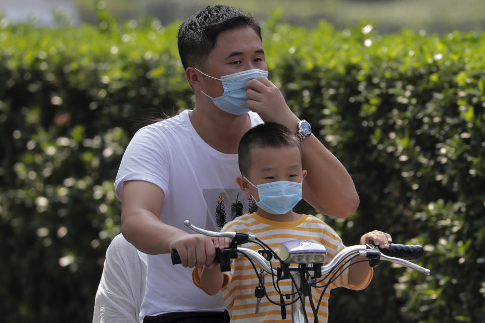 A man and a child wearing face masks to help curb the spread of the coronavirus ride on an electric-powered scooter past the Xinfadi wholesale food market district in Beijing, Sunday, Sept. 6, 2020. According to local news report, Xinfadi market, the capital's biggest wholesale food market have reopen for wholesale operation after it was shutdown following the coronavirus outbreak. China's government on Sunday reported several new coronavirus infections, all believed to have been acquired abroad, and no deaths. (AP Photo/Andy Wong)