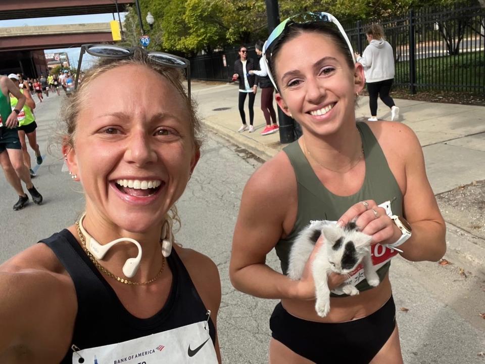 Two runners pose for a selfie, one of them holding a black-and-white kitten.