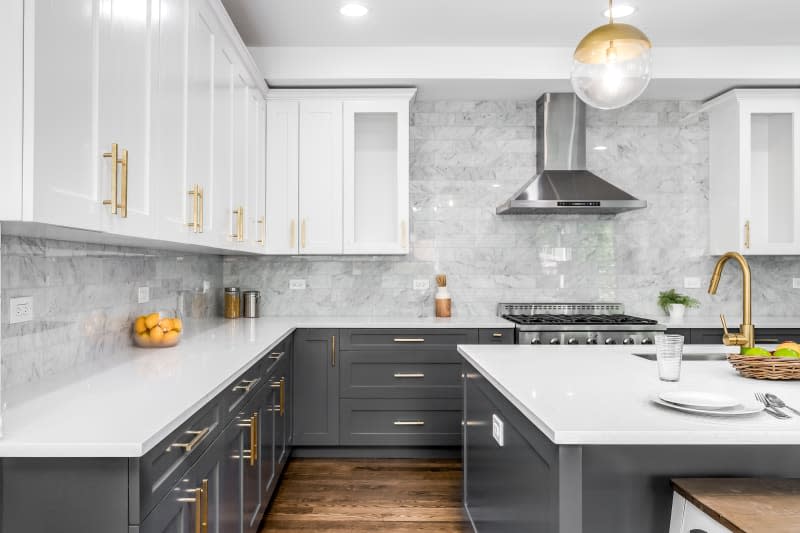 CHICAGO, IL, USA - JUNE 8, 2020: A luxurious white and grey kitchen with gold hardware, Bosch and Samsung stainless steel appliances, and white marbled granite counter tops.