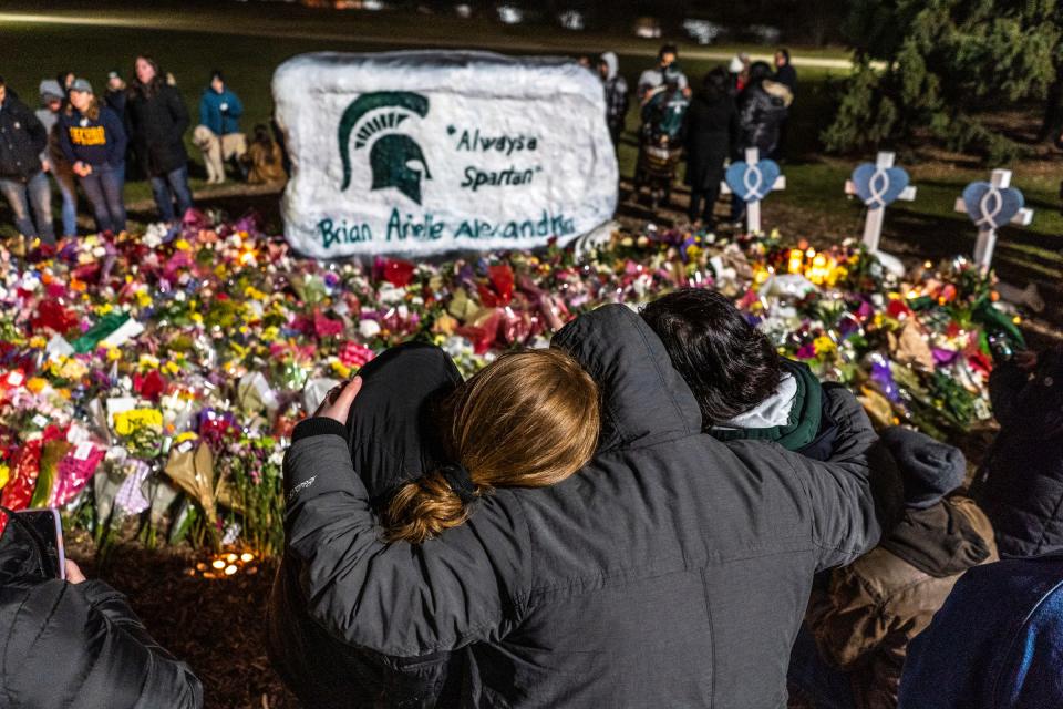 People comfort each other amongst bouquets of flowers during a vigil at the Rock on the Michigan State University campus in East Lansing on Wednesday, Feb.15, 2023, to honor and remember the victims of the mass shooting that happened on the MSU campus that left three dead and multiple others injured.