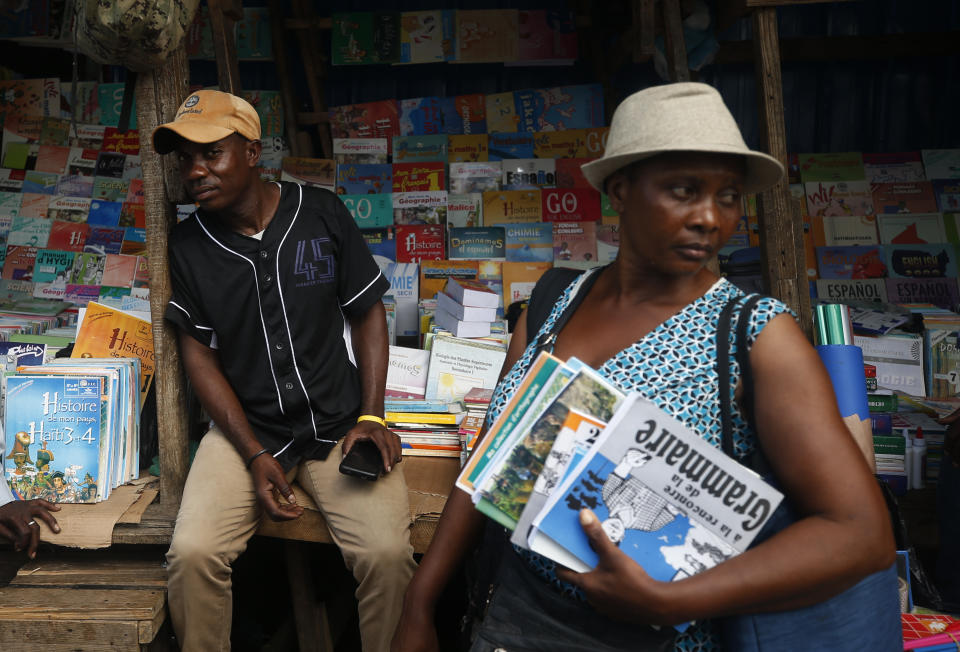 Marcel Cineus, left, keeps an eye on a customer browsing his book stand at a market in Petionville, Port-au-Prince, Haiti, Wednesday, Oct. 2, 2019. School was supposed to start in early September, and Cineus by now would have already sold a couple hundred of books. But violent protests that have shuttered public schools and businesses and left Haiti’s economy sputtering amid ballooning inflation as the opposition demands the resignation of President Jovenel Moïse meant Cineus only sold less than a dozen books last month. (AP Photo/Rebecca Blackwell)