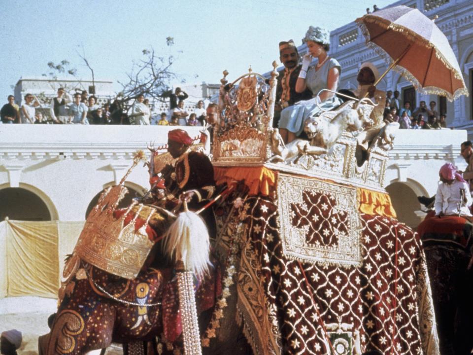 Queen Elizabeth II perches in a howdah on the back of an elephant at Benares, during her tour of India, in 1961.