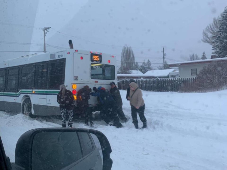 Passengers try to push a bus that was stuck in the snow on 5 Ave. in Prince George, B.C., on Jan. 31, 2023. (Tara Baxter - image credit)