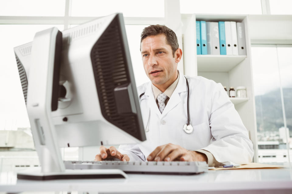 Male doctor working at a desktop computer with a stethoscope hanging on his shoulders.