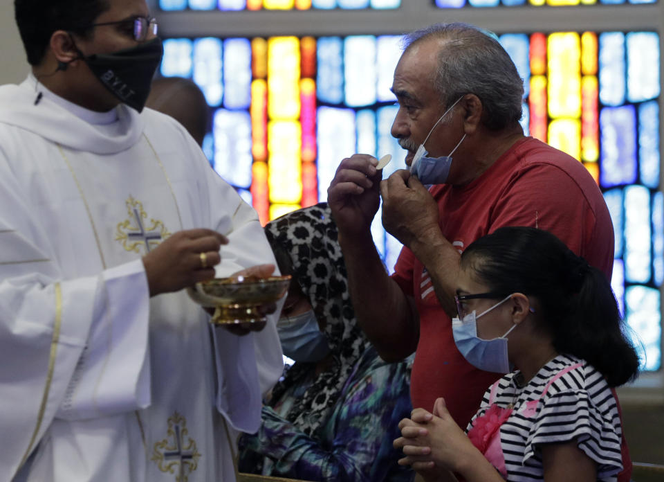 The Rev. Praveen Lakkisettit, left, wears a face mask as he delivers communion to parishioners during an in-person Mass at Christ the King Catholic Church in San Antonio, Tuesday, May 19, 2020.  (Photo: ASSOCIATED PRESS)