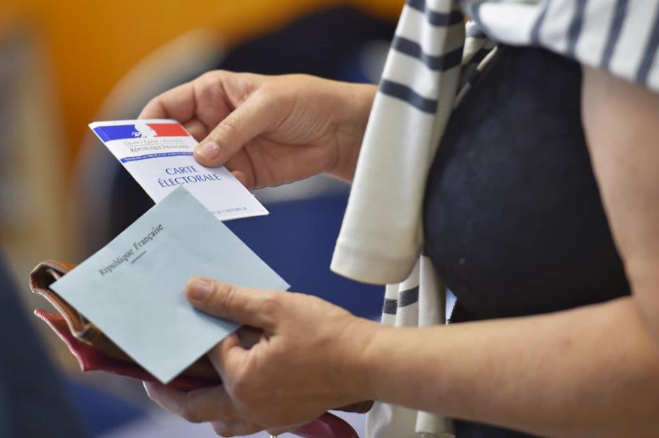 Une femme, carte électorale et enveloppe de vote à la main (Photo d'illustration). - LOIC VENANCE / AFP