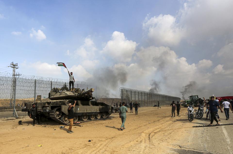 Palestinians wave their national flag and celebrate by a destroyed Israeli tank at the Gaza Strip fence east of Khan Younis southern Saturday, Oct. 7, 2023. The militant Hamas rulers of the Gaza Strip carried out an unprecedented, multi-front attack on Israel at daybreak Saturday, firing thousands of rockets as dozens of Hamas fighters infiltrated the heavily fortified border in several locations by air, land, and sea and catching the country off-guard on a major holiday. 