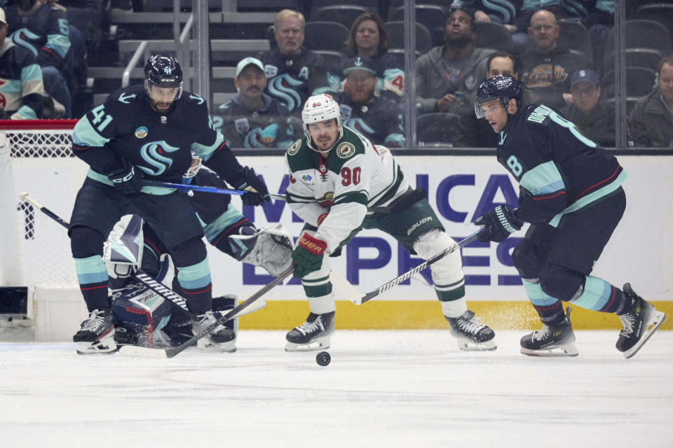 Minnesota Wild left wing Marcus Johansson (90) battles for the puck against Seattle Kraken defenseman Brian Dumoulin (8) and left wing Pierre-Edouard Bellemare (41) during the first period of an NHL hockey game, Sunday, Dec. 10, 2023, in Seattle. (AP Photo/John Froschauer)