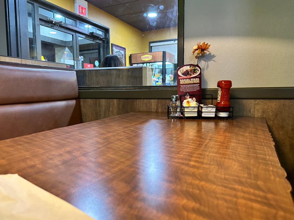 View of Denny's booth, with wooden table and brown cushioned seats