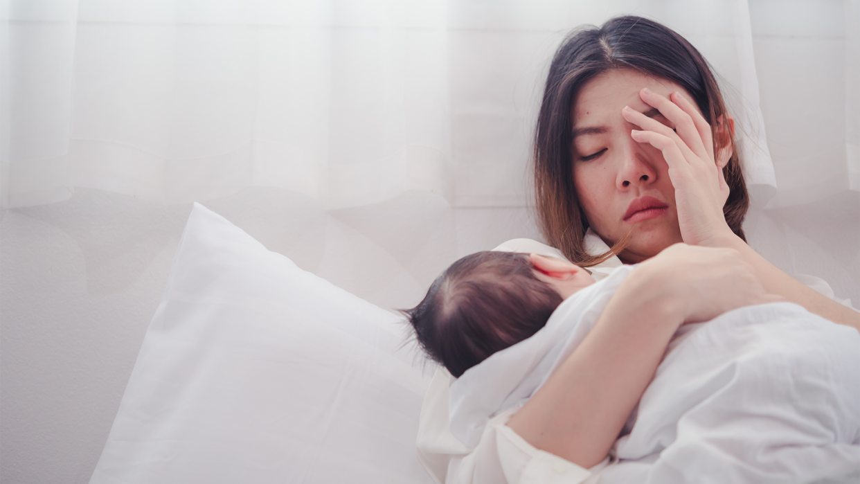Postpartum psychosis represented by a sad-looking mom in white bed holding baby.