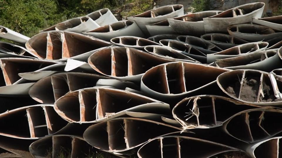 Stacked segments of wind turbine blades showing teardrop-shaped cross-sections with hollow, wooden-looking interior.