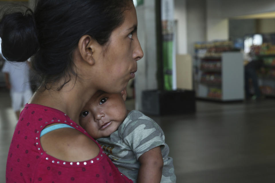 In this July 18, 2019 photo, Maria del Carmen and her 7-month-old baby stand on a sidewalk after being bused by Mexican authorities from Nuevo Laredo to Monterrey, Mexico. Maria del Carmen and her baby was returned from the U.S. side and was met by waiting Mexican immigration officials who handed documents allowing them to work and move about the country. Without further explanation they were then loaded onto chartered buses and sent to Monterrey. (AP Photo/Marco Ugarte)