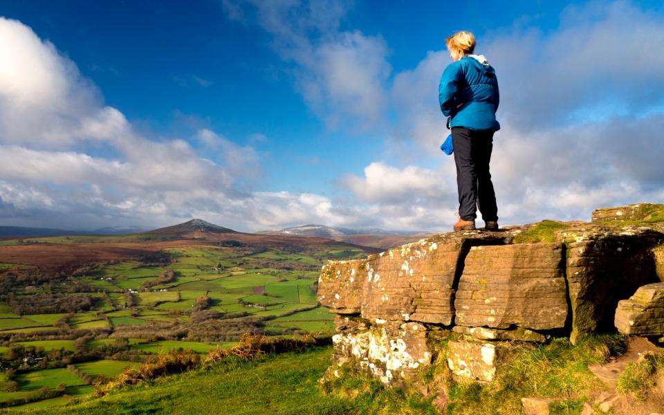 Hiker stands on rocky outrcrop overlooking the landscape - Michael Roberts/Getty Images