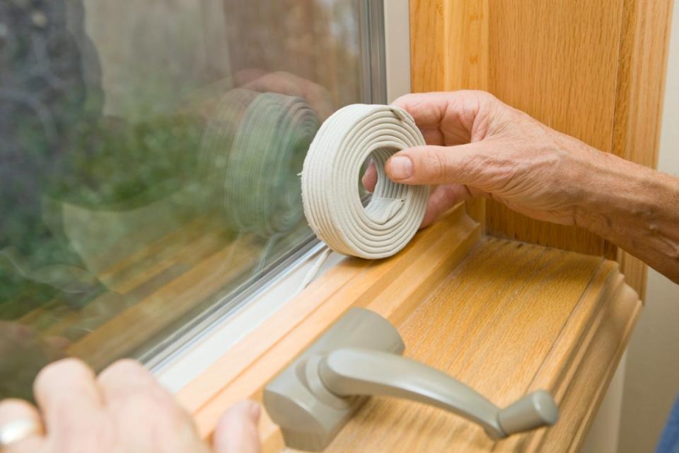 Person adding weather stripping to a wooden window sill.