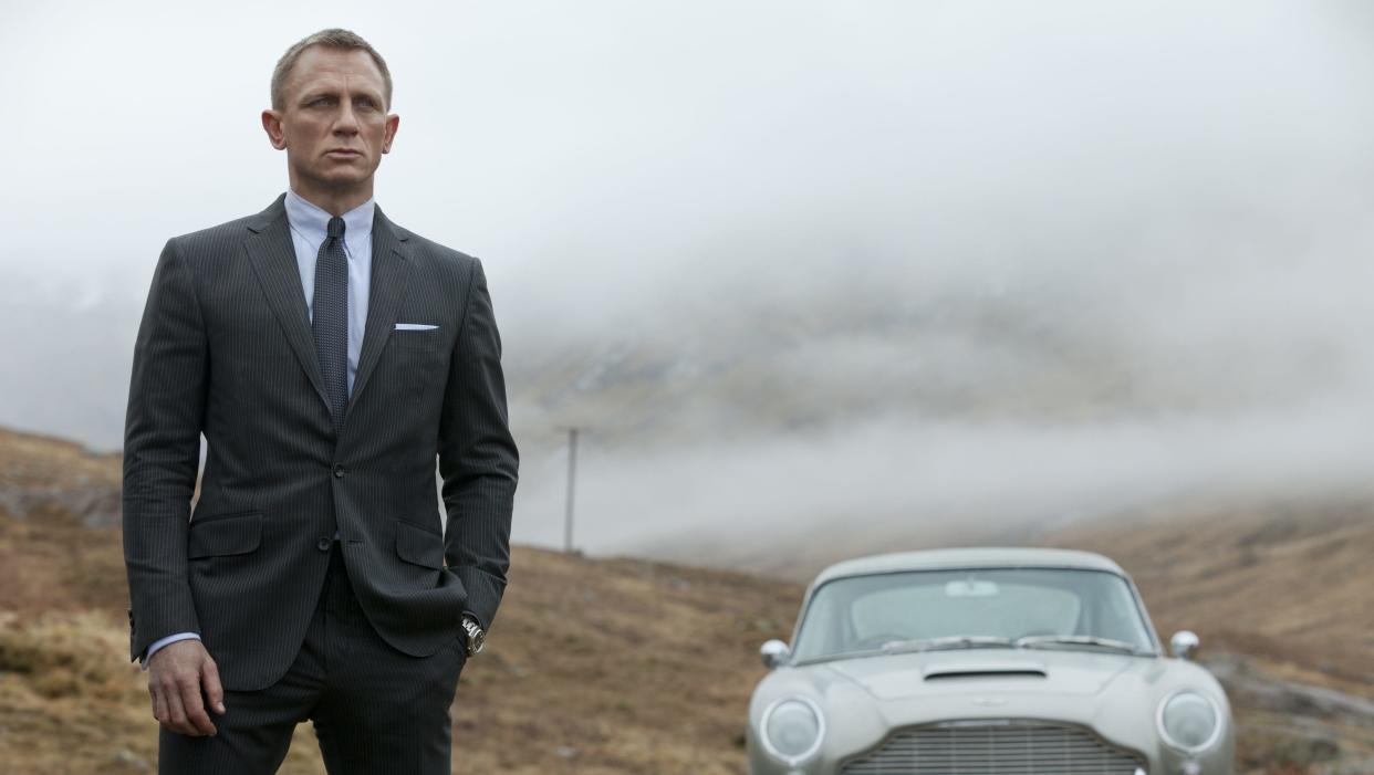  Daniel Craig as James Bond standing next to his Aston Martin in Skyfall. 