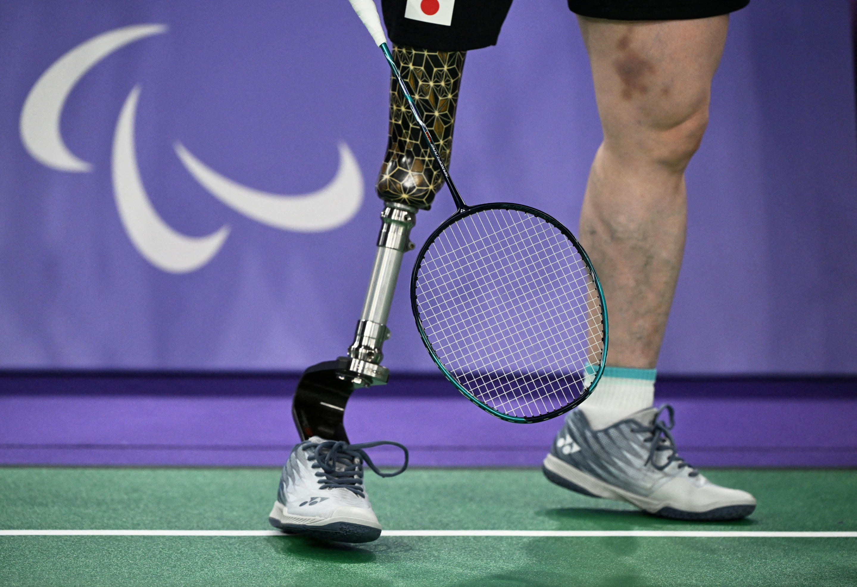 A close-up view of someone with a prosthetic leg on a badminton court.