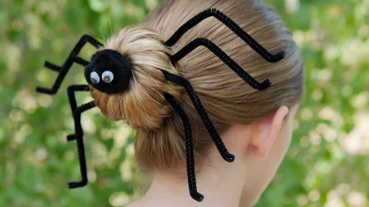 woman wearing a bun hairstyle decorated with black pipe cleaners and googly eyes to resemble a spider for halloween