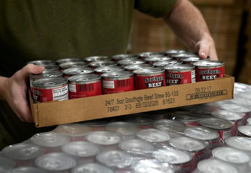 Mike Beagan moves to stack a case of canned beef stew in the production reclamation room of the Rhode Island Community Food Bank.