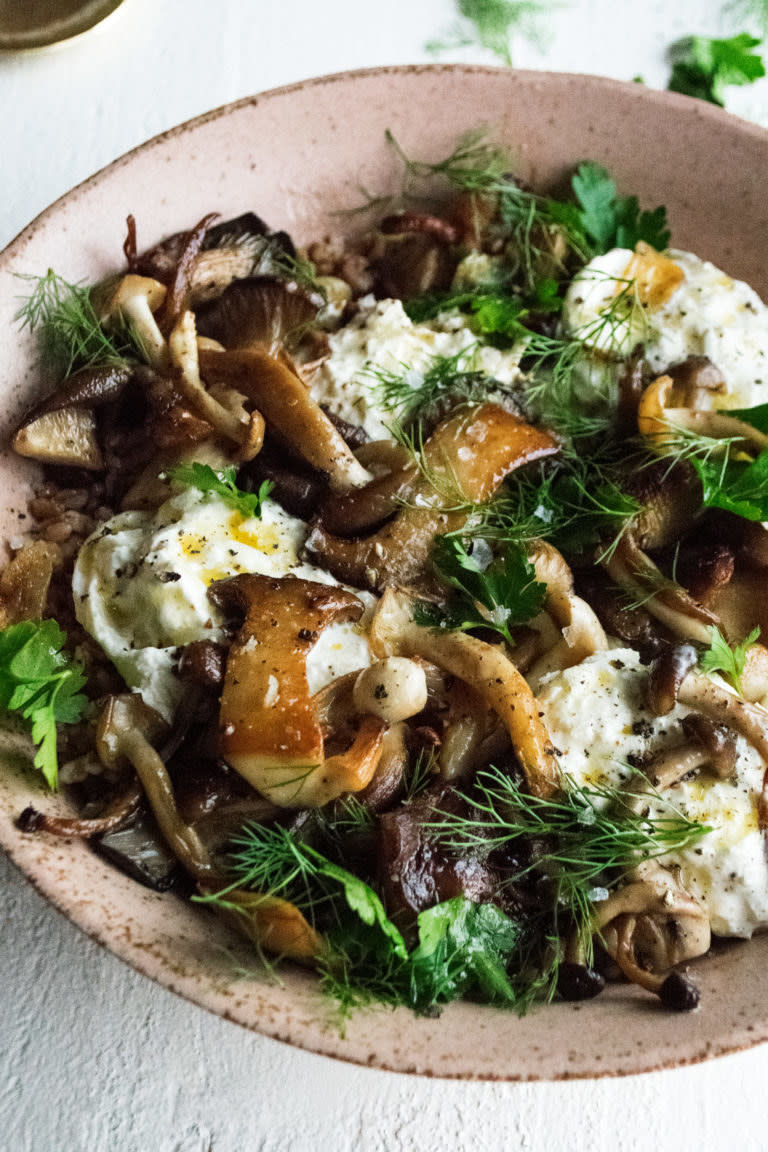 A bowl of mushrooms with burrata and herbs.