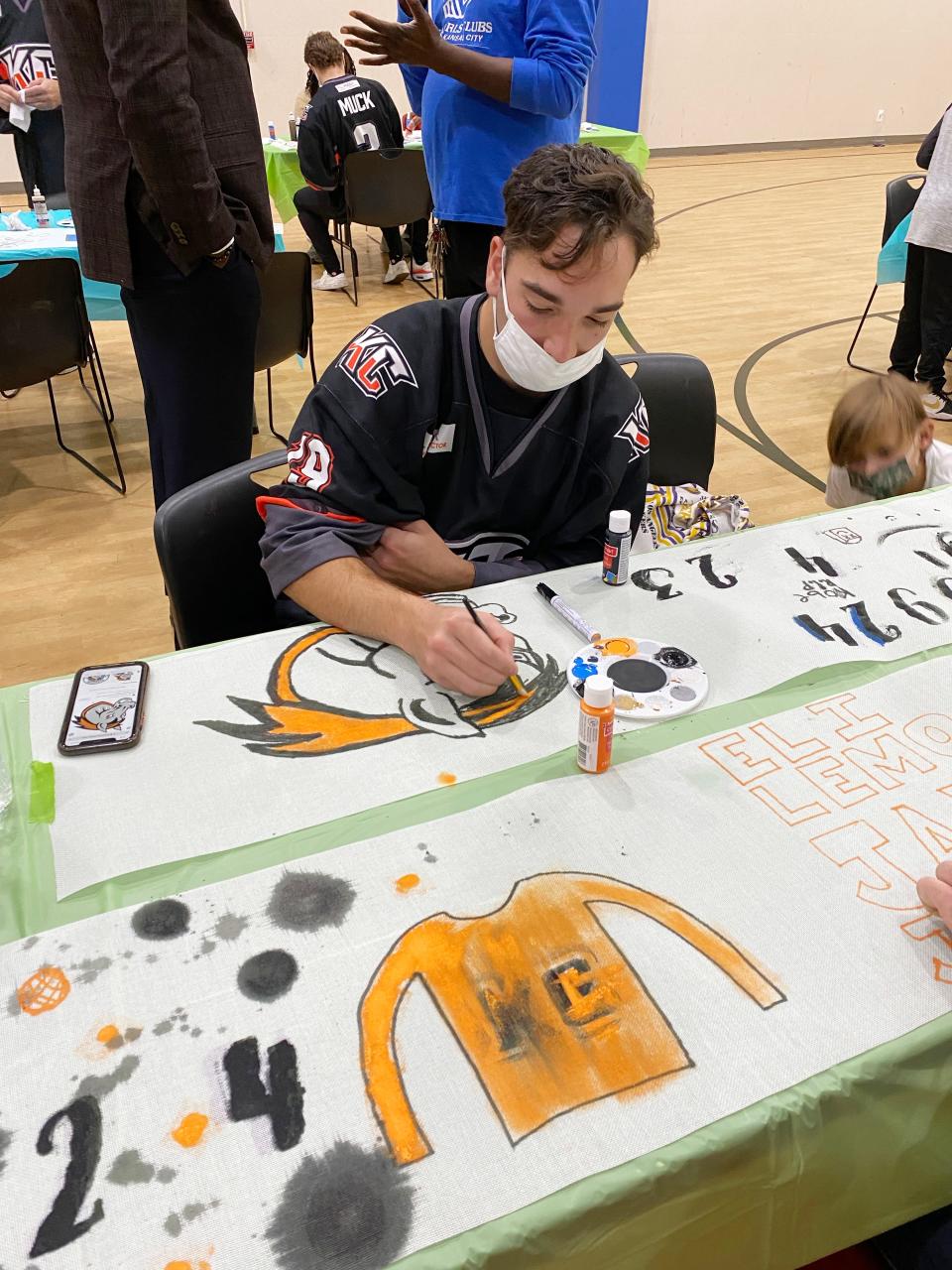 Kansas City Mavericks player Bryan Lemos sketches a portrait of Mac the Mascot on a table runner that will be used and auctioned off at the upcoming Dinner on Ice event, to benefit area Boys & Girls clubs. Lemos and his teammates visited the Independence branch Wednesday afternoon to paint and visit with some of the children.