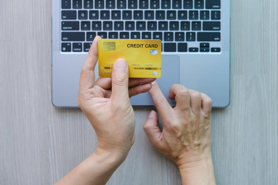 A hand holding a credit card over a laptop