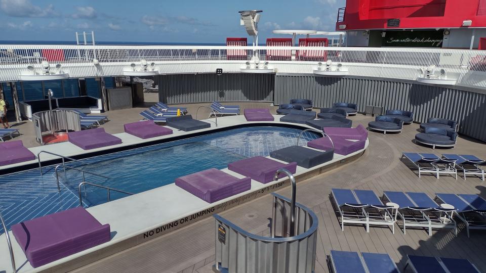 A cruise ship pool surrounded by chairs and daybeds.