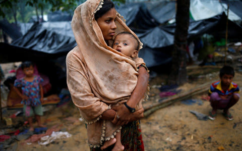 A Rohingya refugee woman wraps her child with a scarf as it drizzles in Cox's Bazar, Bangladesh - Credit: REUTERS/Mohammad Ponir Hossain