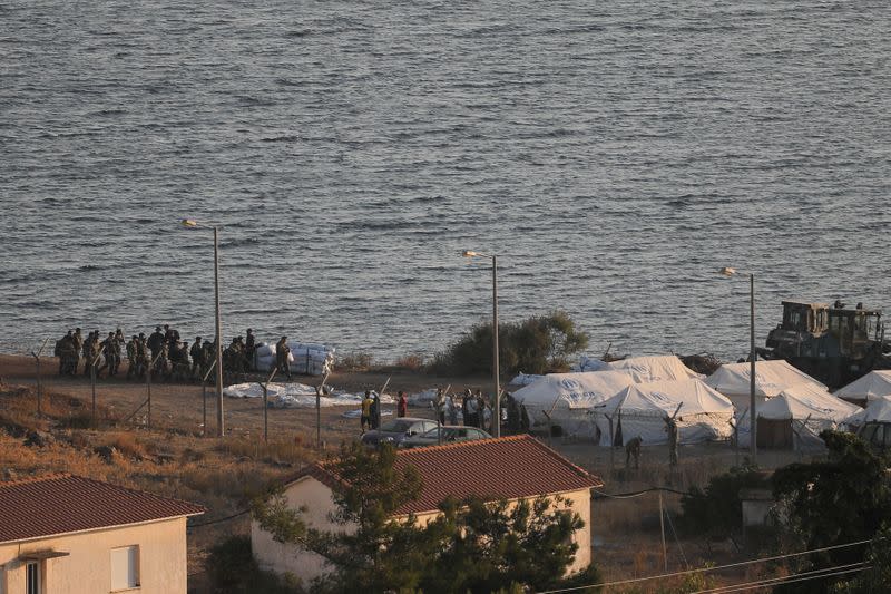 Migrants from the destroyed Moria camp and officials stand next to tents as Greek soldiers arrive at a new temporary camp, on the island of Lesbos