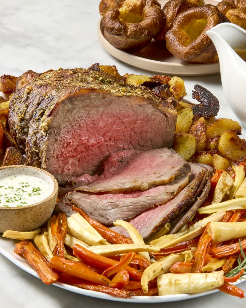 side shot of a serving platter with a full roast beef, roasted carrots and crispy potatoes.